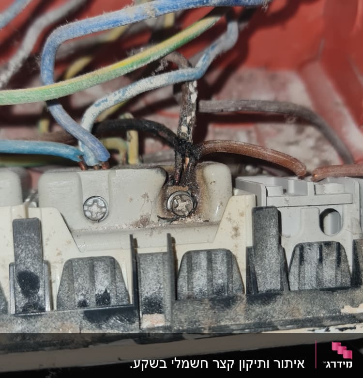 חוטי חשמל צבעוניים מחוברים לקופסת חיבורים עם סימני שריפה